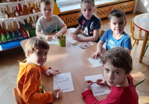 Dzieci przy stoliku rysują dinozaury po śladach